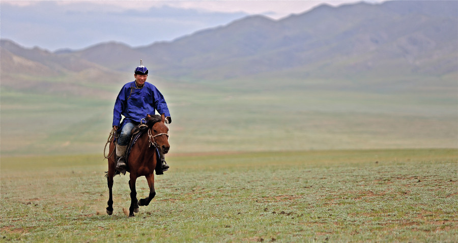 Ein mongolischer Reiter in blauem Gewand vor einer Berglandschaft.